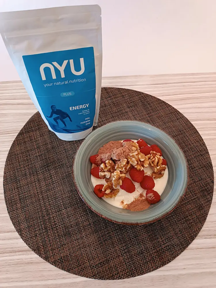 energy plus by Nyu Eco.
Un bol de yogur con una bolsa de Nyu Eco detrás, un cuenco de frambuesas, otro de nueces y otro con el producto, un polvo muy similar al cacao, en un tercero.